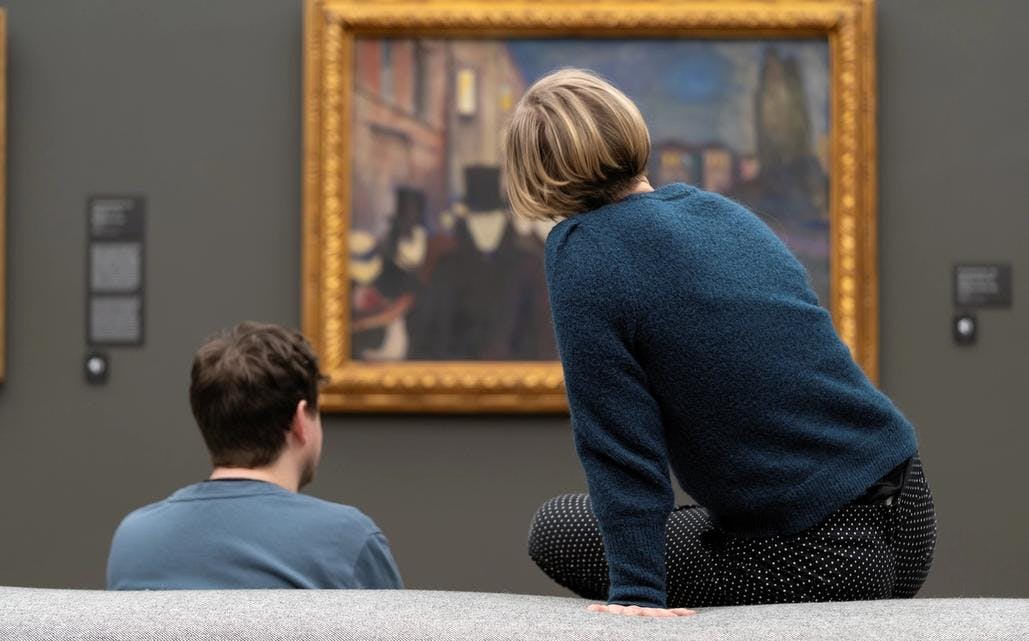 Bilde av en kvinne og mann som sitter sammen foran et stort Munch-maleri. 