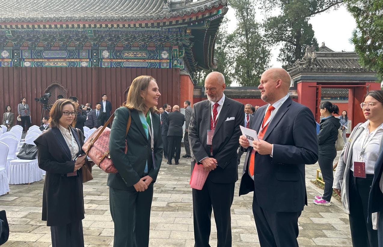 To kvinner og to menn i dress som snakker sammen foran et kinesisk tempel.