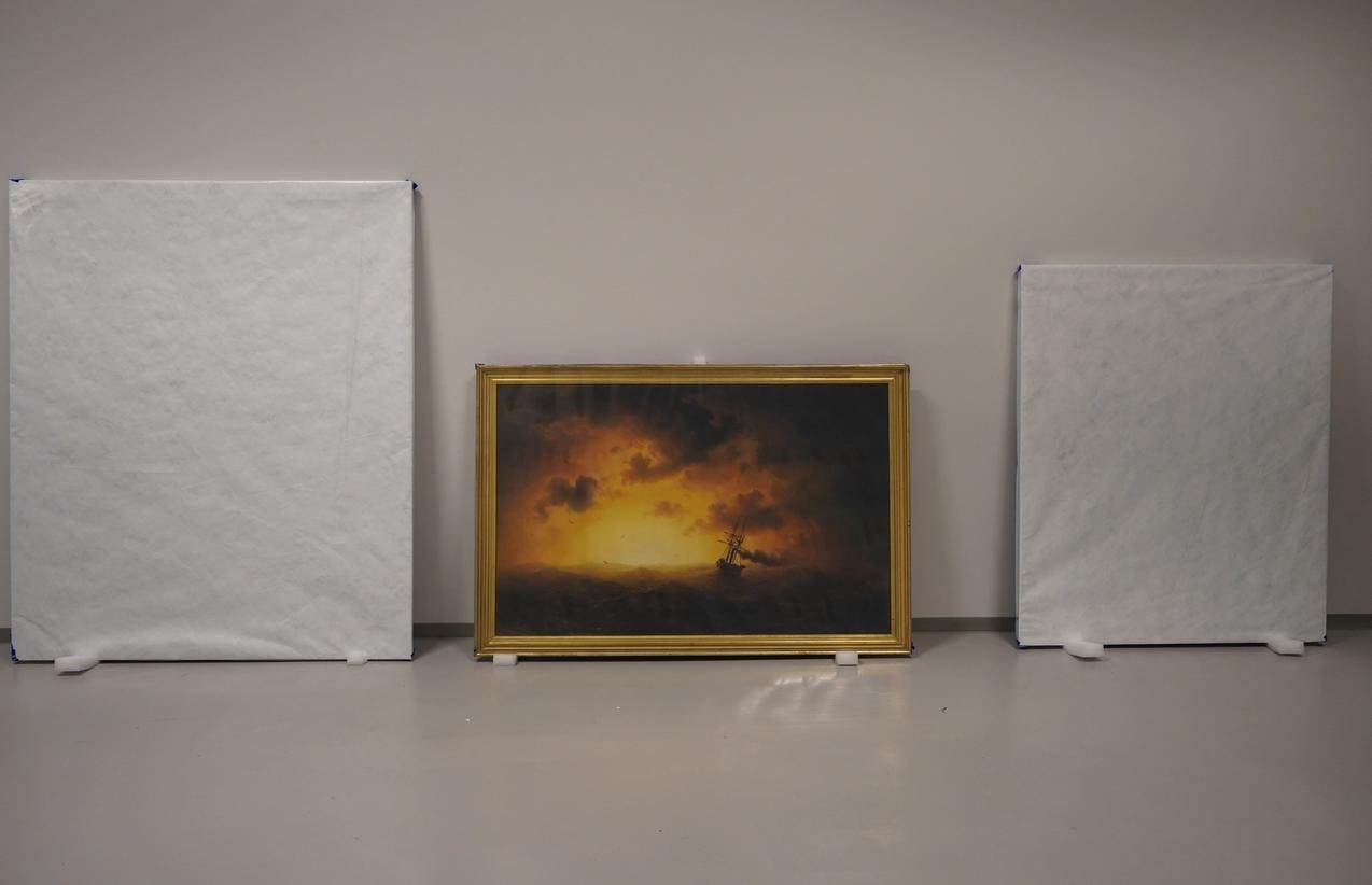 Et maleri står midt mellom to bilder pakket inn i hvitt papir