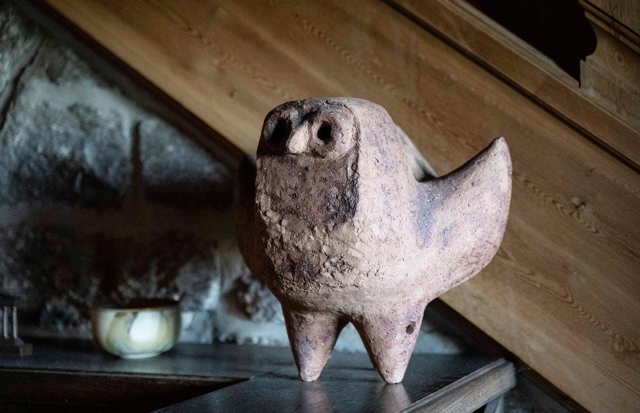 En skulptur i keramikk av en ugle, som står på en bokhylle.