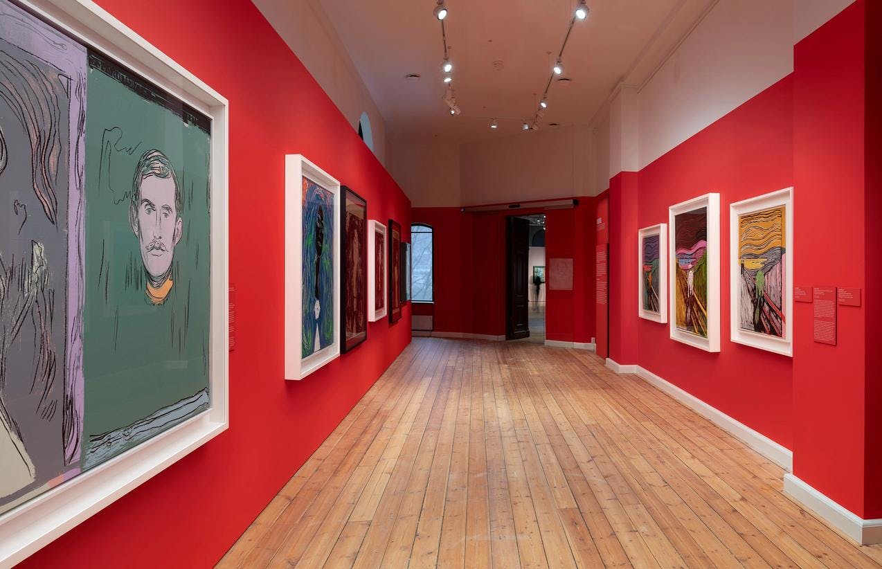 An exhibition room with bright red walls, where colorful works by Andy Warhol are displayed.