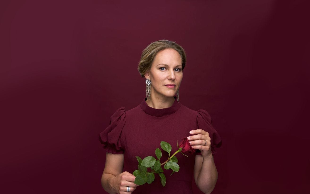 Portrettfoto av Ingeborg Gillebo som holder en langstilket rød rose, kledt i dyp rød kjole. 