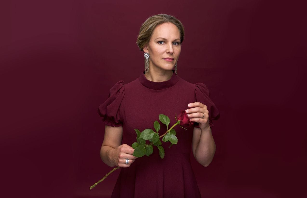 Portrettfoto av Ingeborg Gillebo som holder en langstilket rød rose, kledt i dyp rød kjole. 