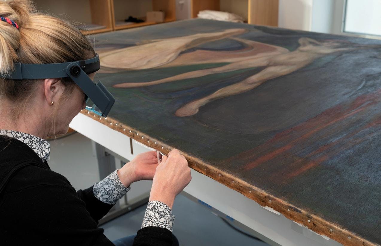 A person in sitting in front of a painting by Edvard Munch. She is working on conservation.