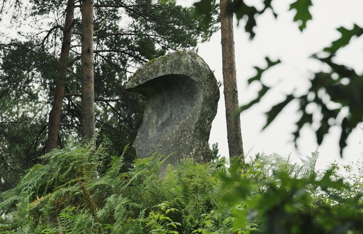 En stor stein formet som en bauta, mellom grønt gress og trær. 