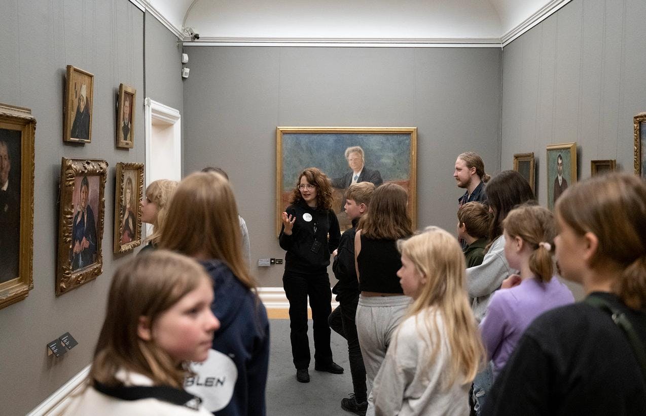 Photograph from the Rasmus Meyer's collection depicting a guide talking to a group of visitors in front of exhibited paintings.