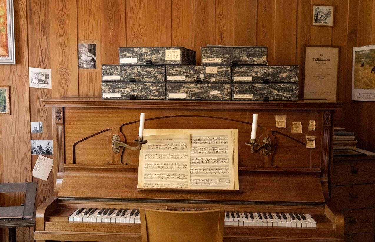 Et brunt piano med et oppslått noteark, og flere grå esker plassert oppå pianoet.