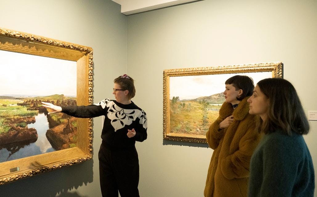 Et bilde av tre kvinner som ser på et maleri, den ene kvinnen peker og forteller noe.