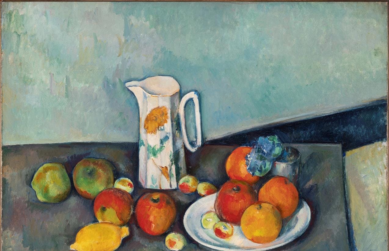 Et maleri av Cézanne som viser et stilleben på et bord. Vi ser en hvit kanne med blomstermotiv, et fat med appelsiner, epler og en liten vase med en blå blomst oppå. På bordet ligger flere epler, plommer og en sitron. Bakgrunnen er ensfarget lys turkis med synlige malingsstrøk.