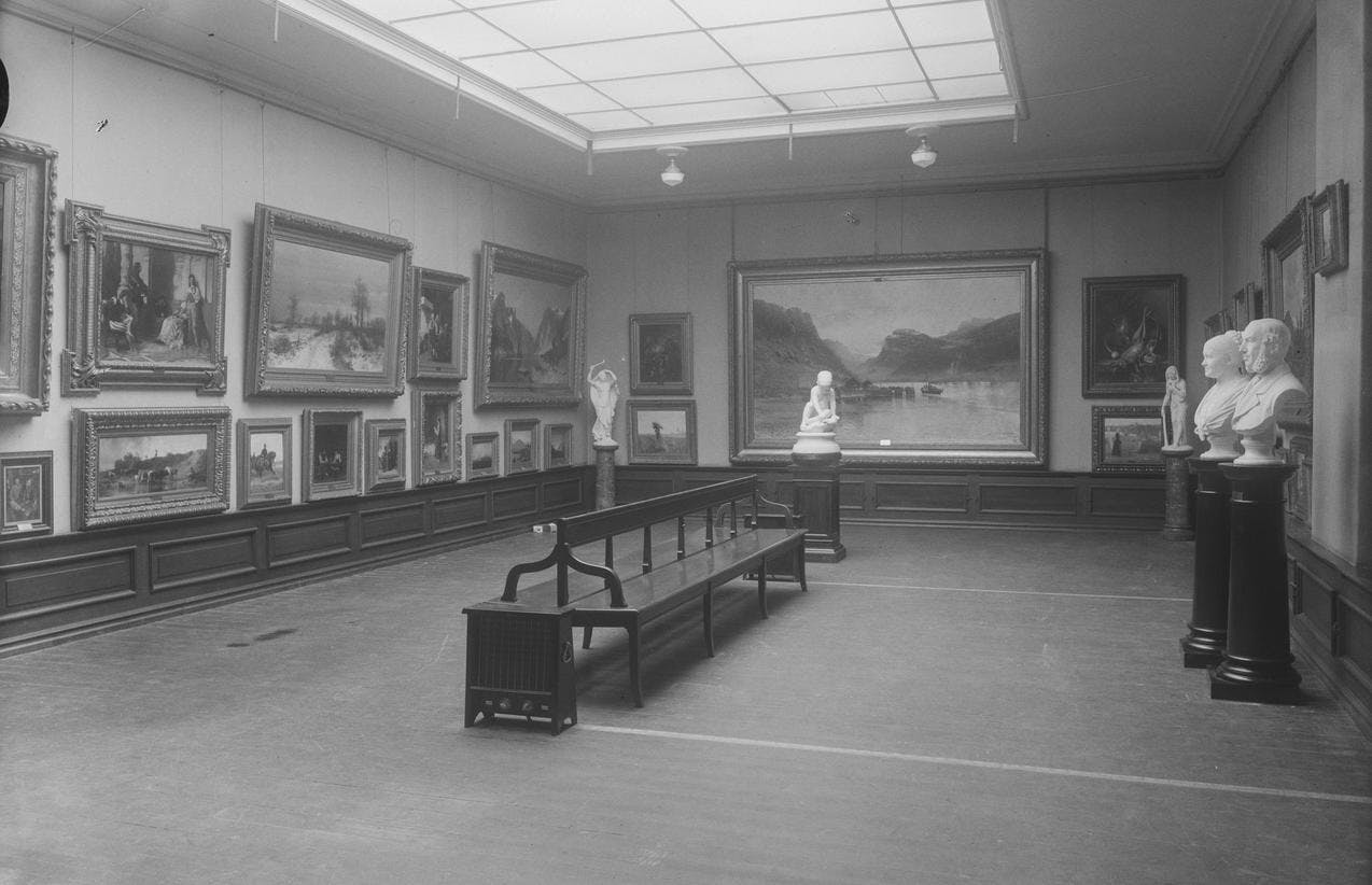 Gammelt fotografi fra utstillingssalen i Bergen billedgalleri som viser en sal med tett i tett med malerier på veggen.
