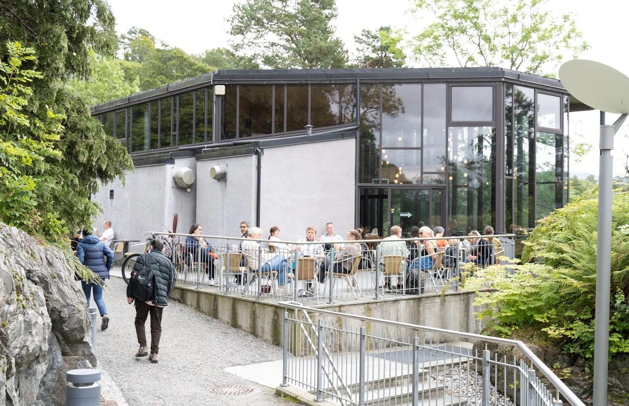 Uteområdet ved museet på Troldhaugen, med kafebord og mange mennesker sittende rundt.