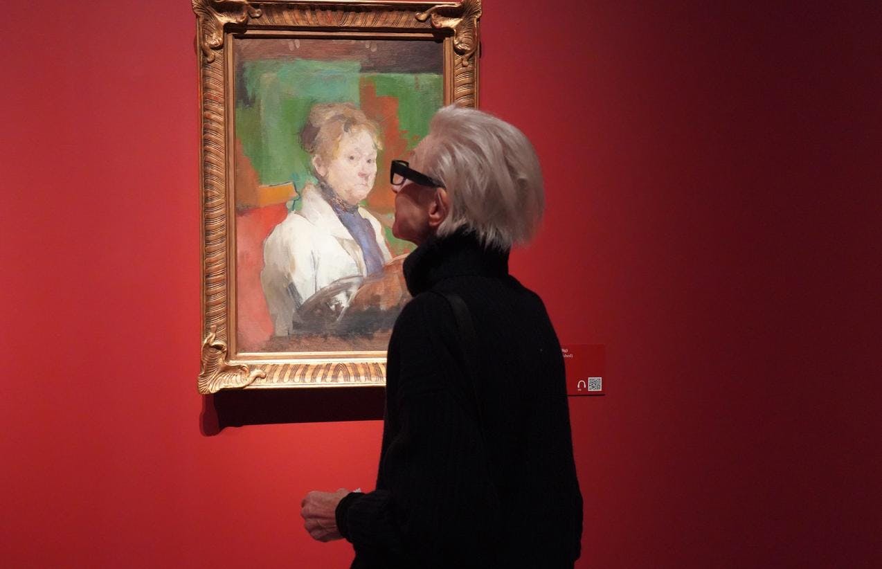 En kvinne foran et maleri av Harriet Backer, på en rød utstillingsvegg