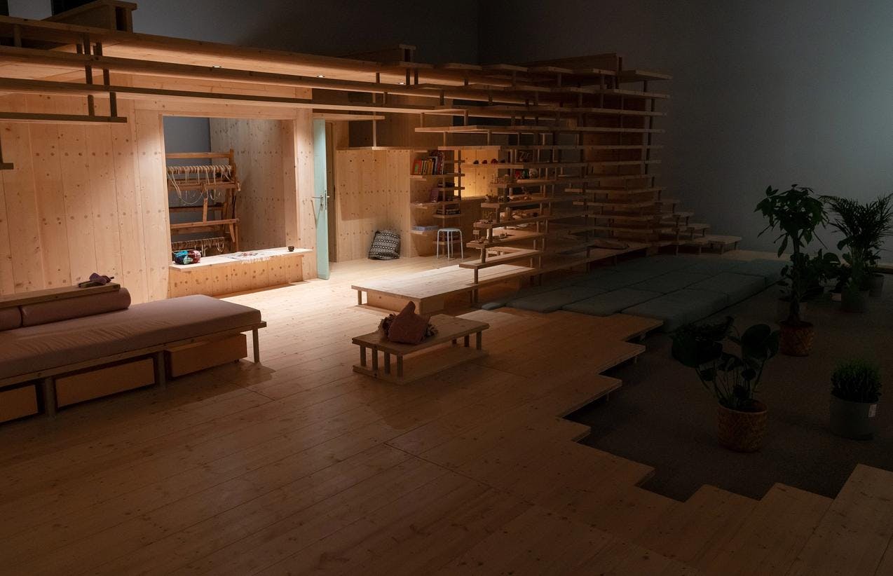 Foto fra utstillingen Nabo som viser et overblikk, du ser hyllestrukturer i tre og små rom, blant annet et hobbyrom med vev og en sovealkove.