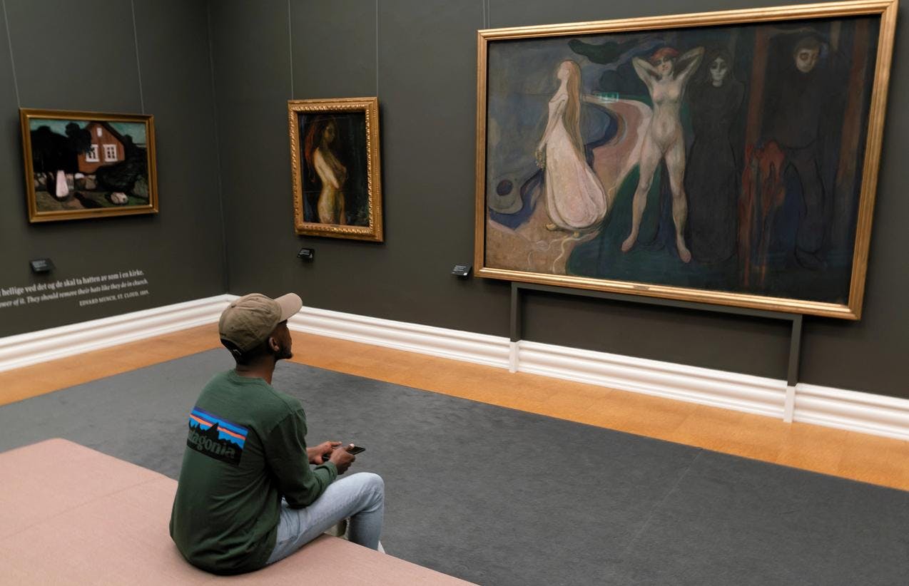 En mann sitter foran et maleri av Edvard Munch