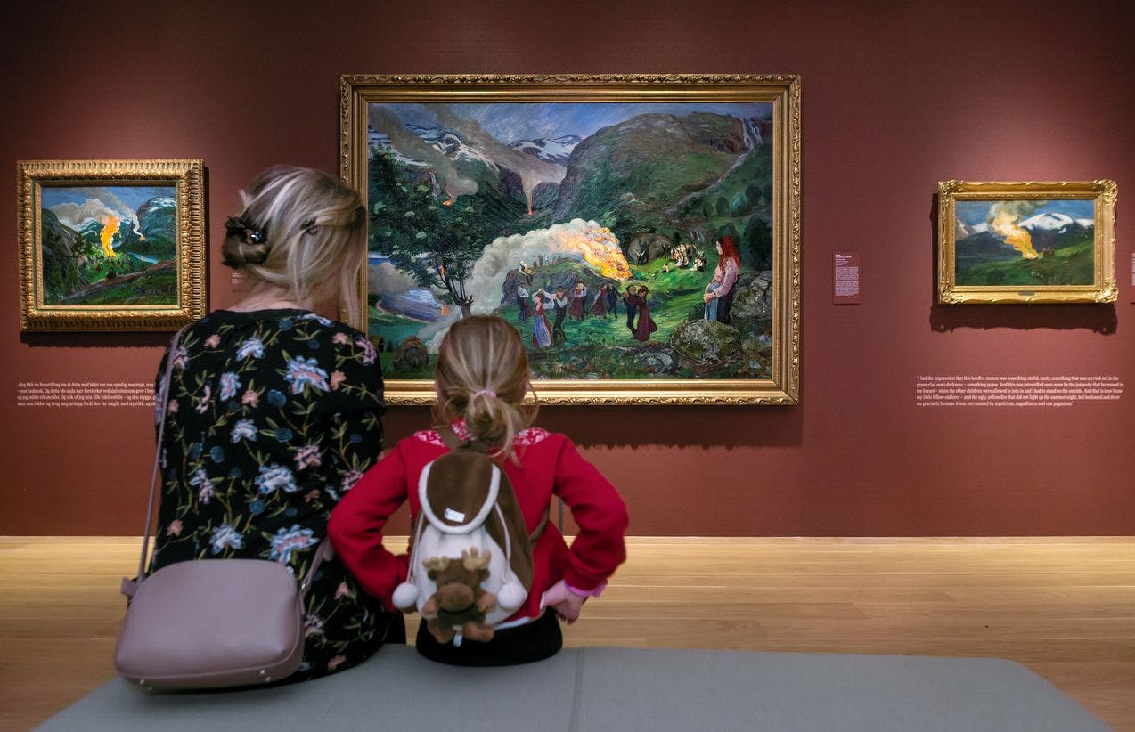 A woman and a child are sitting in front of a painting by Nikolai Astrup