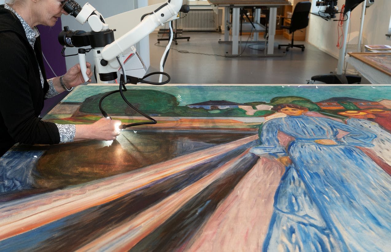 En person som arbeider med konservering av et maleri av Edvard Munch