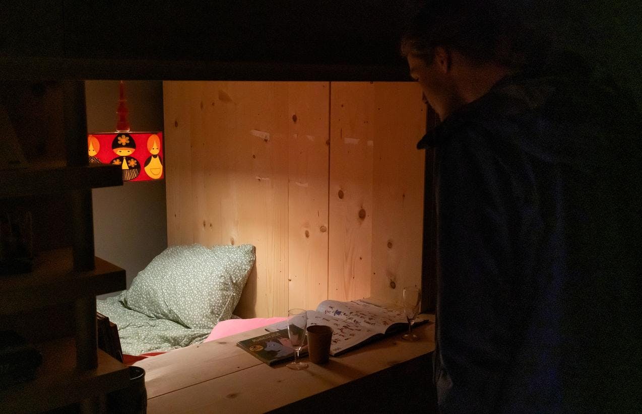 Et bilde fra utstillingen Nabo som viser en person som titter inn i sovealkove.