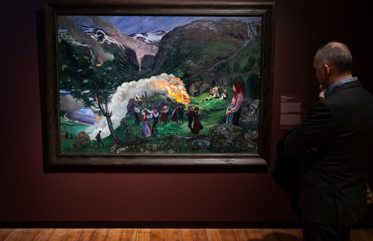 En mann står til høyre foran et maleri av Nikolai Astrup, i utstillingen Brikker