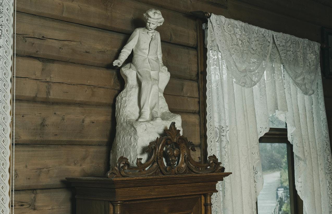 En hvit liten skulptur av Edvard Grieg er plassert oppå et skap, inne i Griegs villa