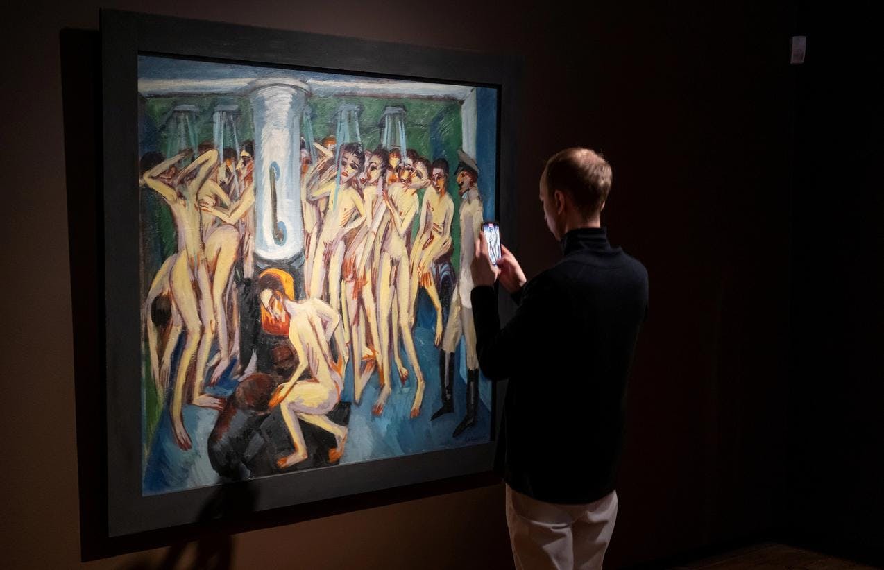 En mann står foran et maleri, som framstiller nakne soldater. Han tar bilde av maleriet.