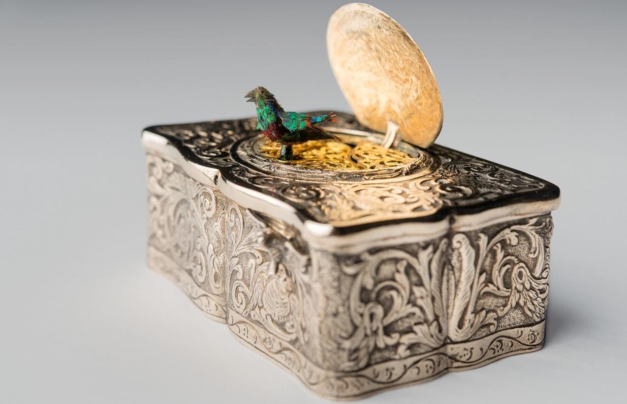 En spilledåse i sølv med en liten fugl montert på lokket
