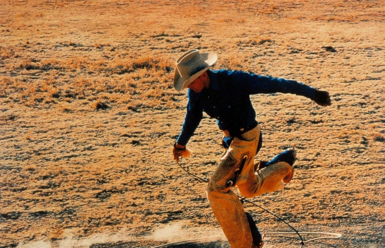 Et foto av en cowboy i ørkenen som hopper med lasso