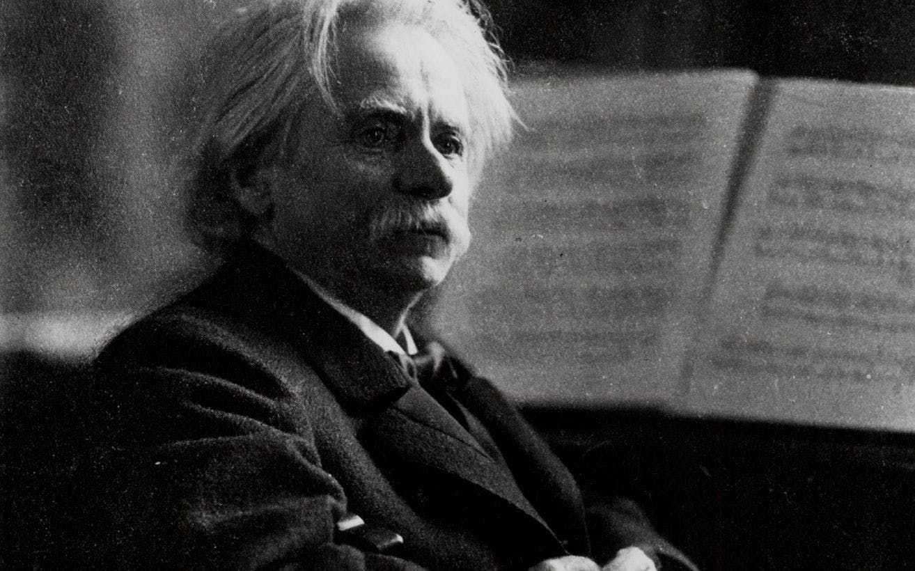 Sort-hvitt foto av Edvard Grieg. Han ser mot høyre og har armene i fold.